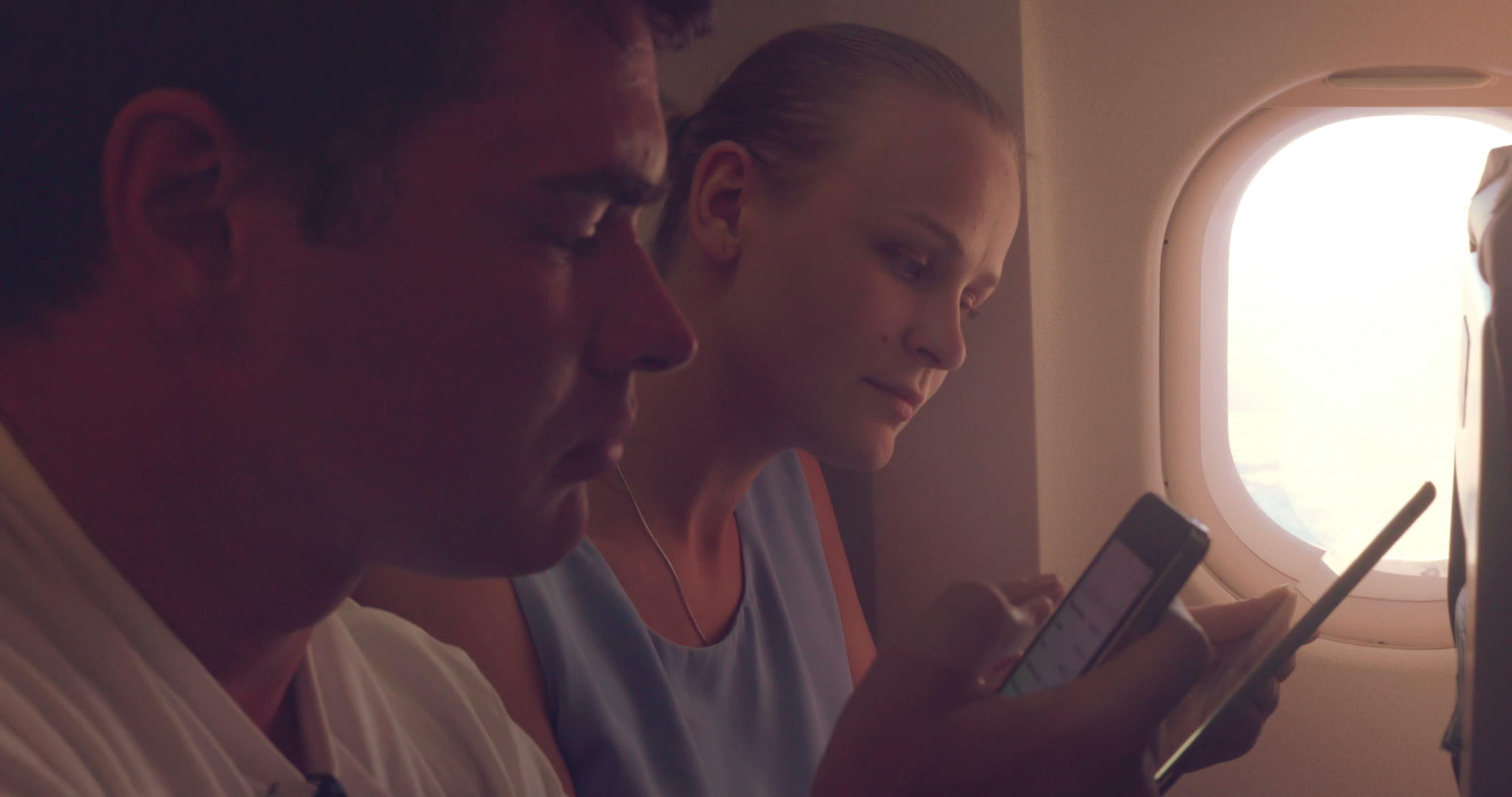 年轻人在飞机上使用平板电脑和手机视频的预览图