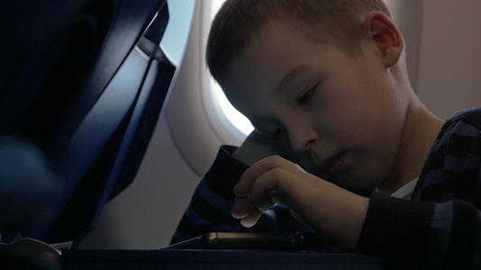 一个小男孩坐在飞机上在手机上玩游戏视频的预览图