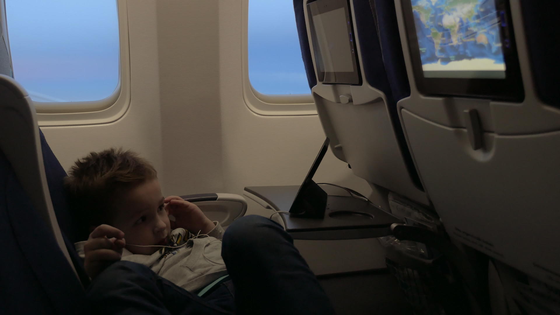小男孩戴着耳机在飞机窗口的座位上看电影视频的预览图