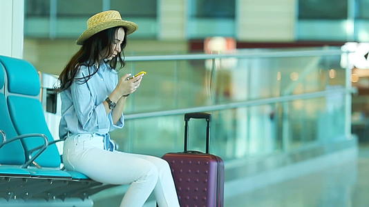 一名年轻女子在机场休息室等飞机在候诊室里拿着智能手机视频的预览图