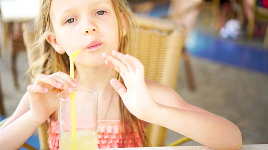可爱的小女孩坐在晚餐桌旁喝着新鲜的果汁视频的预览图