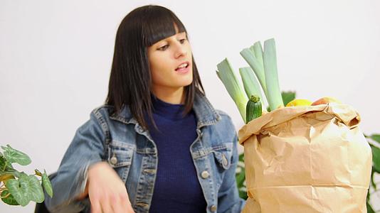 一个黑头发的年轻女人拿着一袋蔬菜购物袋吃着一个苹果视频的预览图