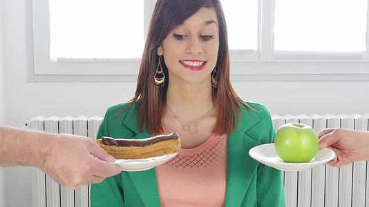 年轻女性在苹果和巧克力蛋糕之间选择一个视频的预览图