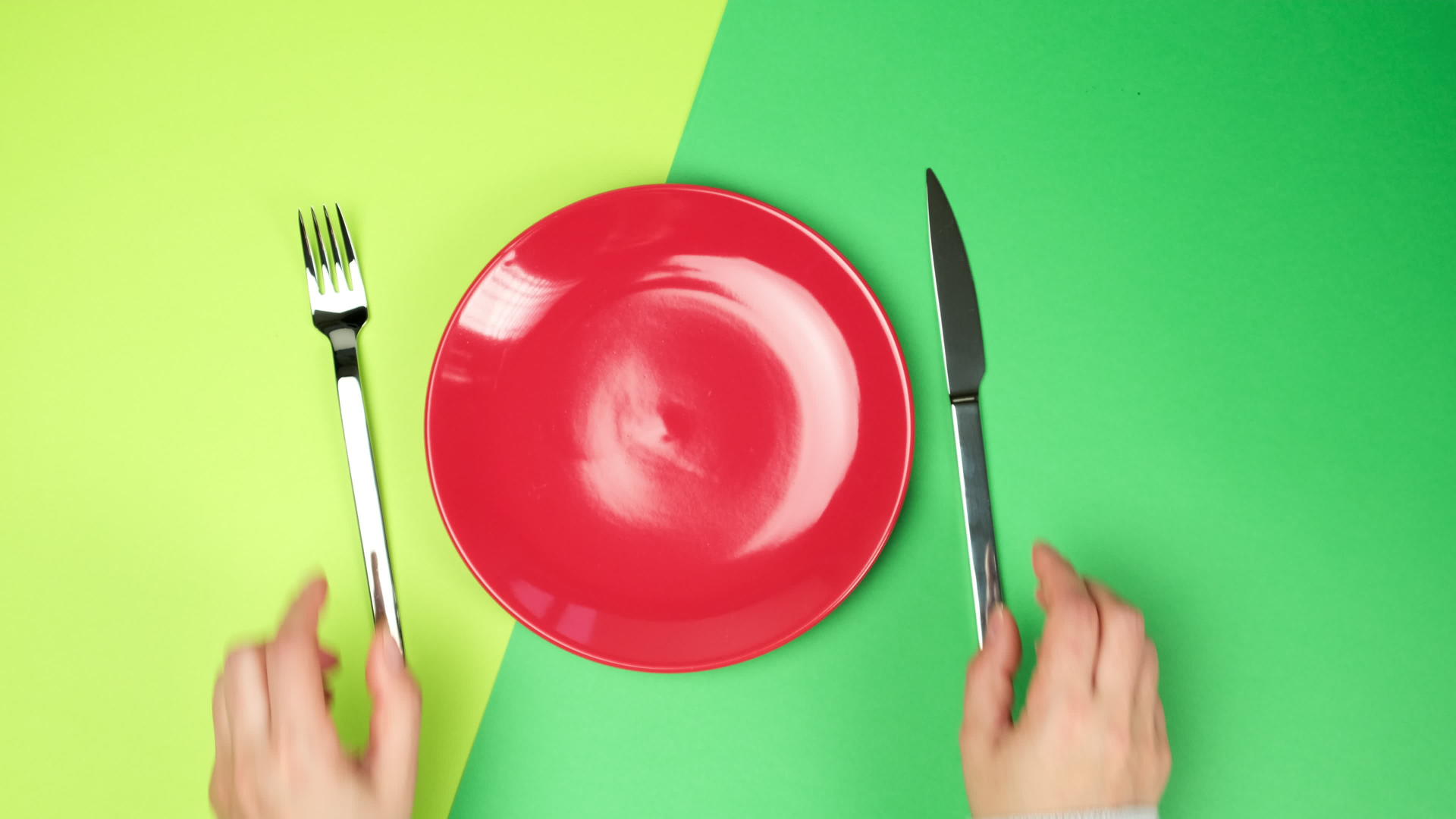 女人把手放在绿色背景金属叉和刀子上靠近一个空的红色圆形陶瓷视频的预览图