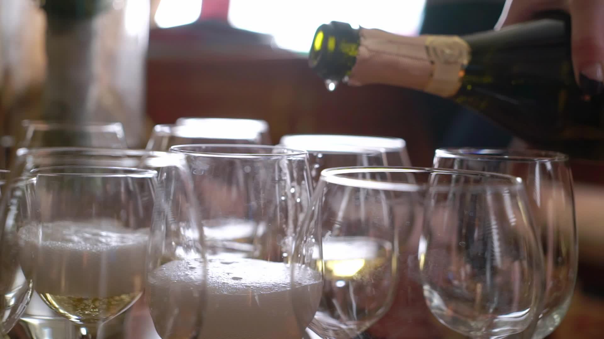 把香槟从瓶子倒到桌子上的空杯子里视频的预览图