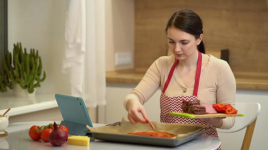 女厨师准备披萨看在线食谱在平台上看平板电脑视频的预览图