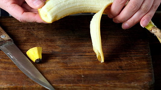 在棕色切割板上切一块新鲜的黄色香蕉头皮和切片视频的预览图