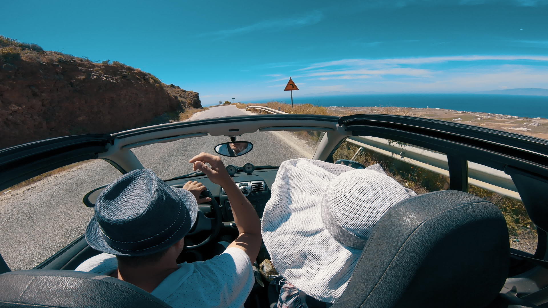 一对夫妇沿着海岸公路驾驶敞篷车前往希腊圣托里尼视频的预览图