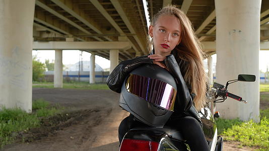 骑摩托车的女孩戴着摩托车头盔坐在城市汽车桥下的摩托车桥下视频的预览图