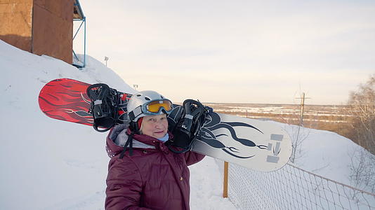身着雪板的高级女子在冬山雪度假胜地散步视频的预览图