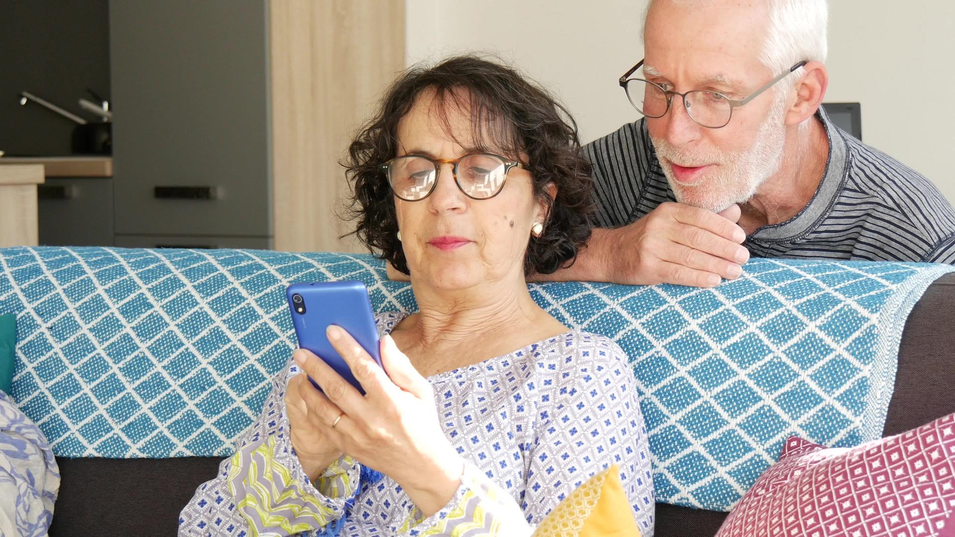 一对成熟吸引力的夫妇使用智能手机坐在沙发上视频的预览图