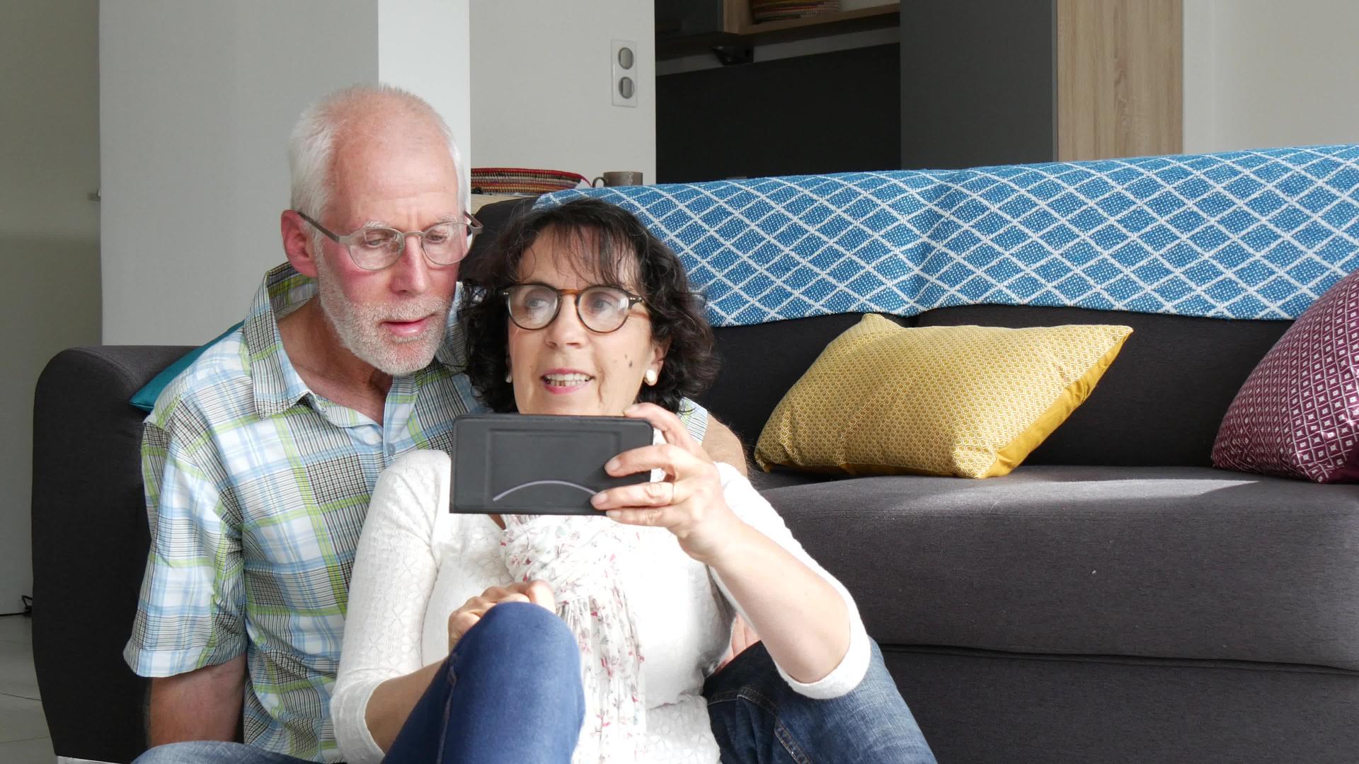 一对成熟吸引力的夫妇使用智能手机坐在沙发上视频的预览图