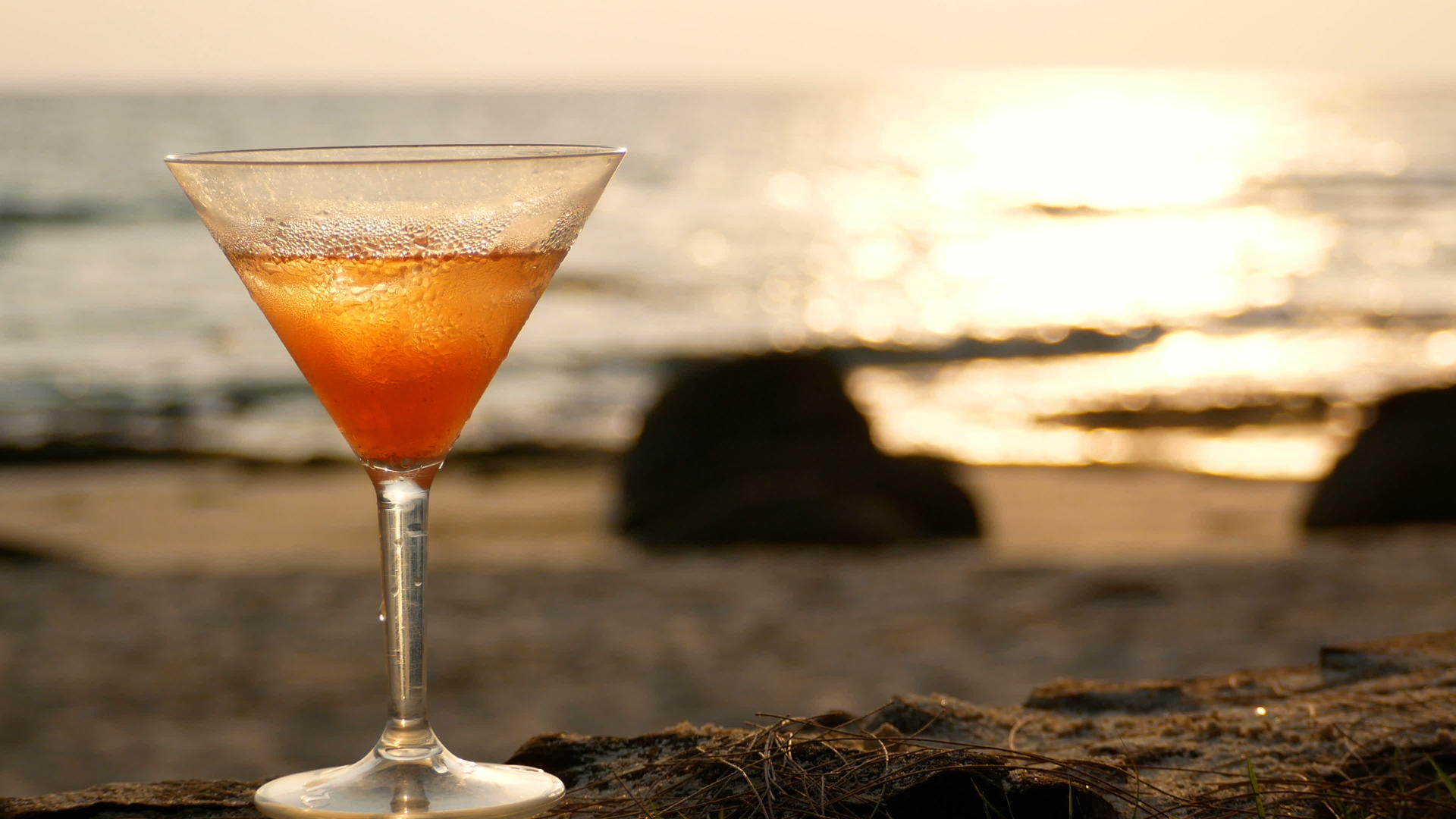 4k海滩上有水滴的鸡尾酒杯在日落时反射金波视频的预览图