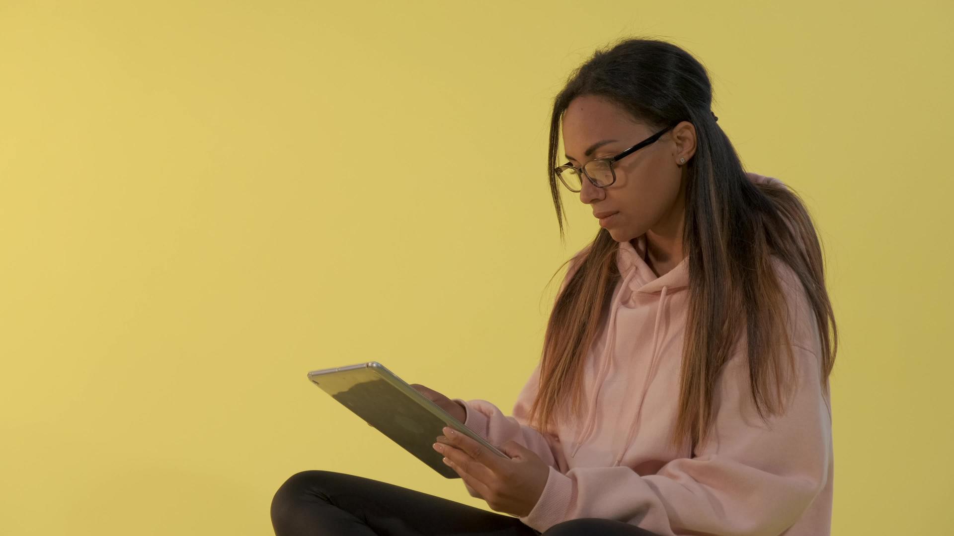 黑人黑人妇女在黄色背景的平板电脑上工作戴着眼镜视频的预览图