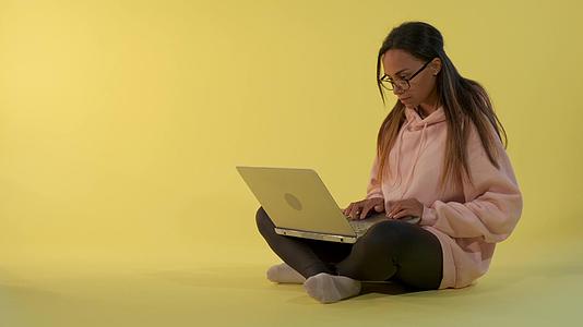 精明的非洲女孩在黄色背景下从事计算机工作视频的预览图