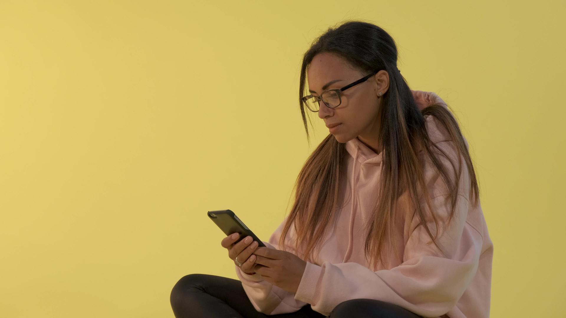 在智能手机上工作的眼镜中黑人女性的特写视频的预览图