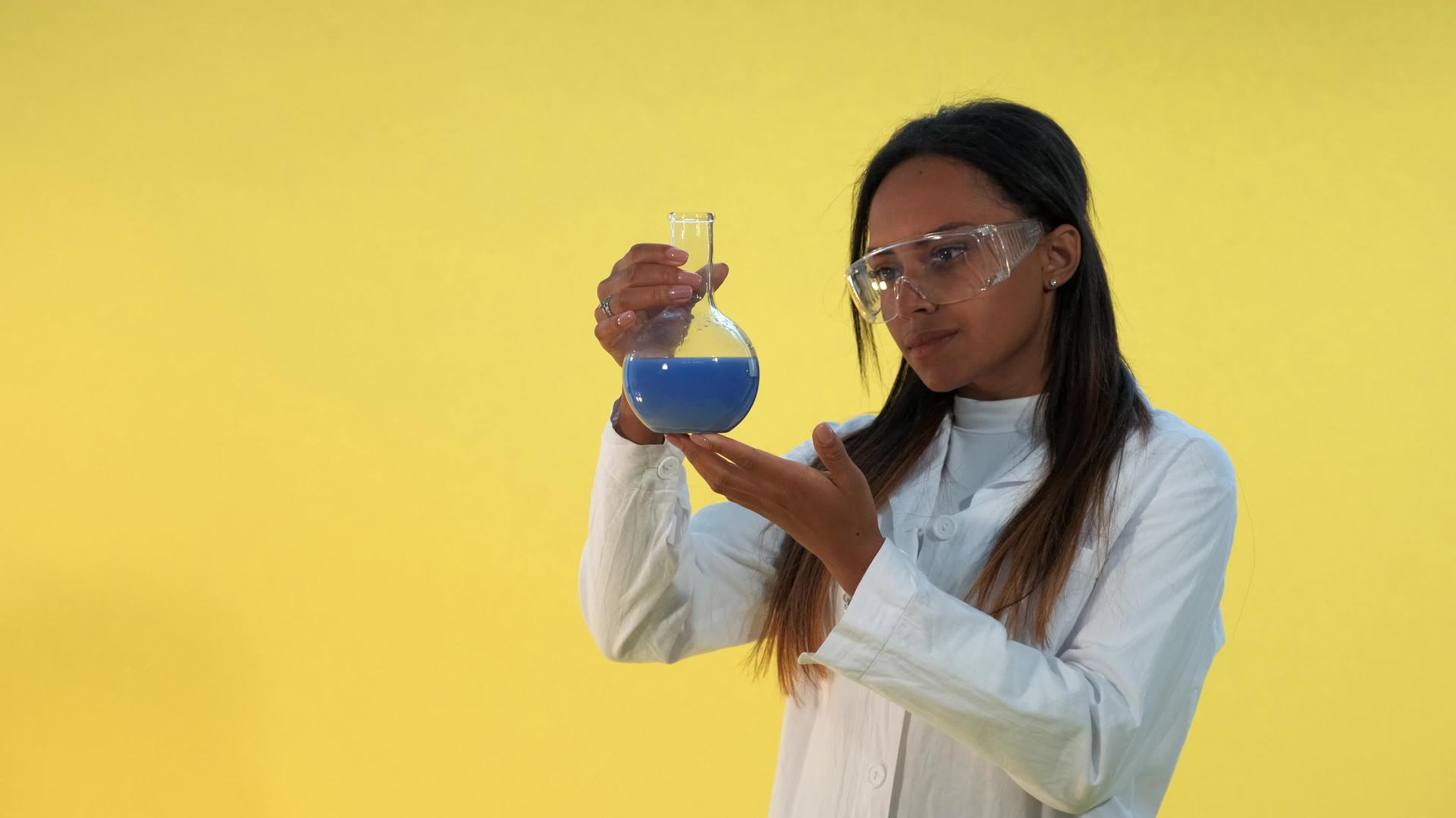 美丽的黑人戴着安全眼镜和实验室外套手里拿着一个含有液体的酒瓶视频的预览图
