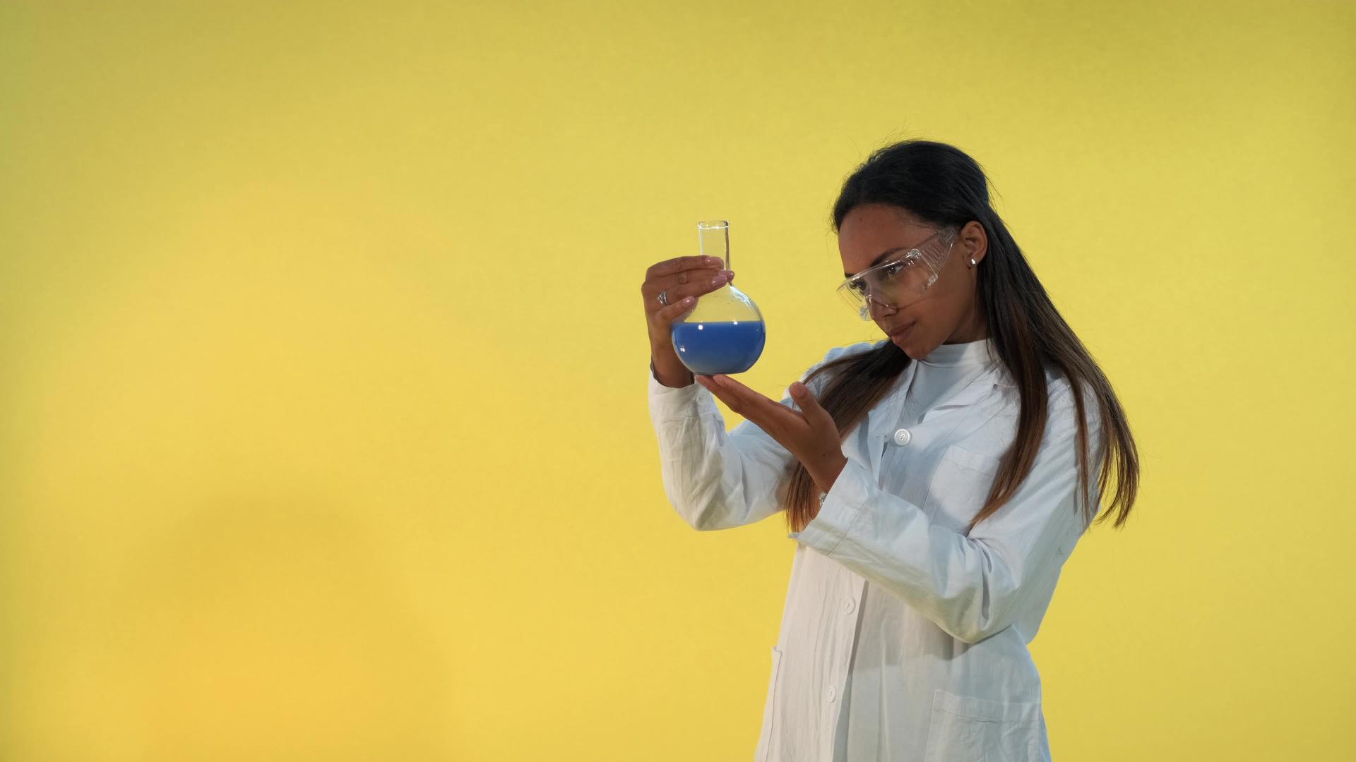 黑人女科学家穿着实验室外套在黄色背景上使用实验液体视频的预览图