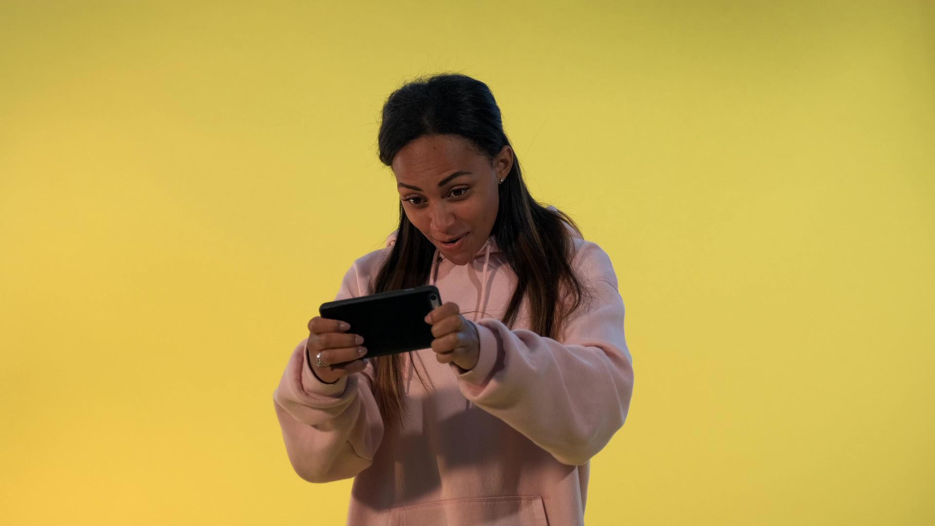 美丽的黑人女孩在黄色背景的智能手机上玩游戏视频的预览图