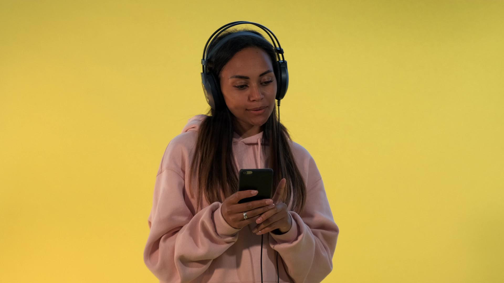 多民族幸福的多民族妇女在黄色背景下用耳机听音乐视频的预览图
