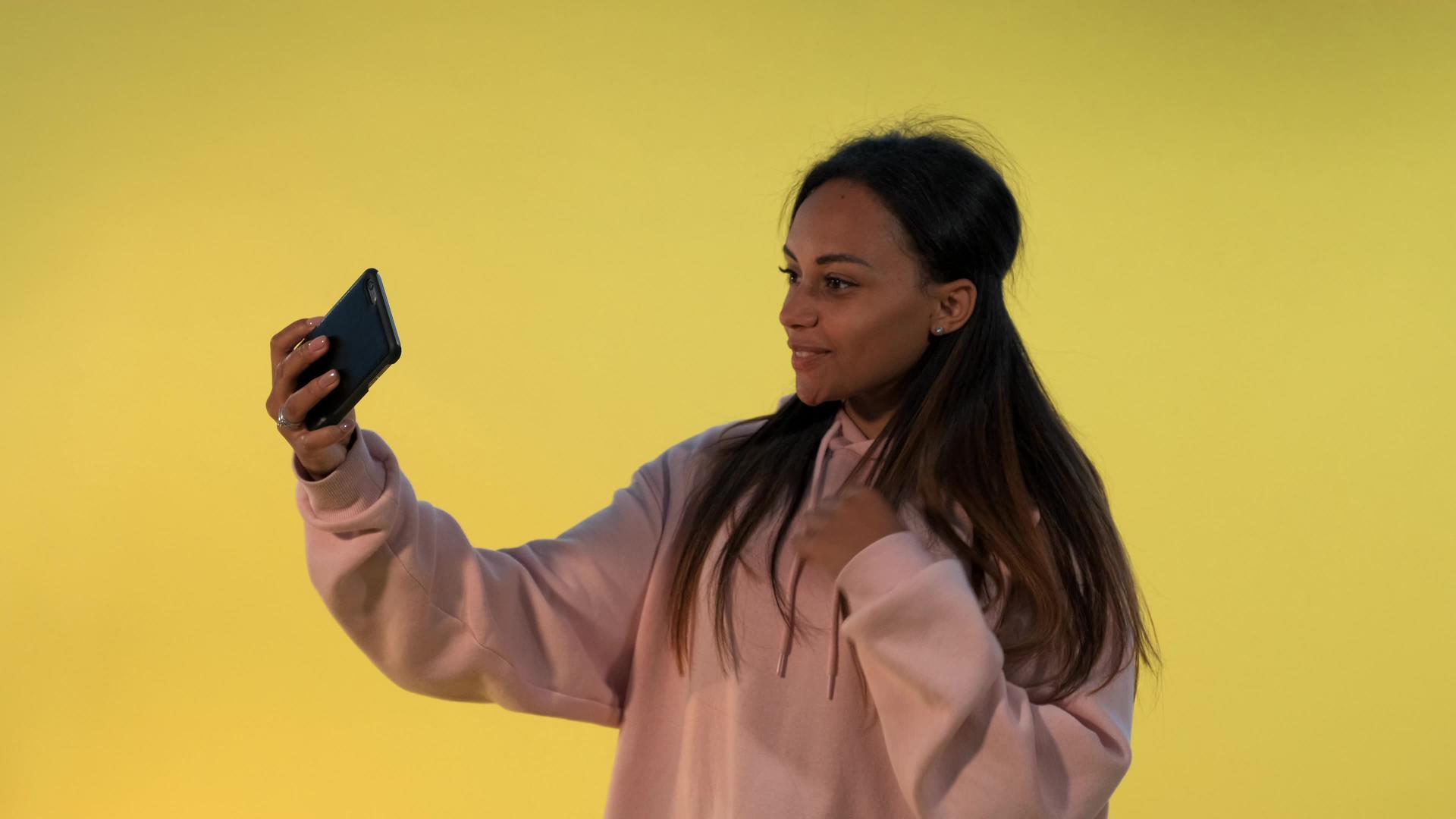 在黄色背景的智能手机上自拍的混血女孩视频的预览图