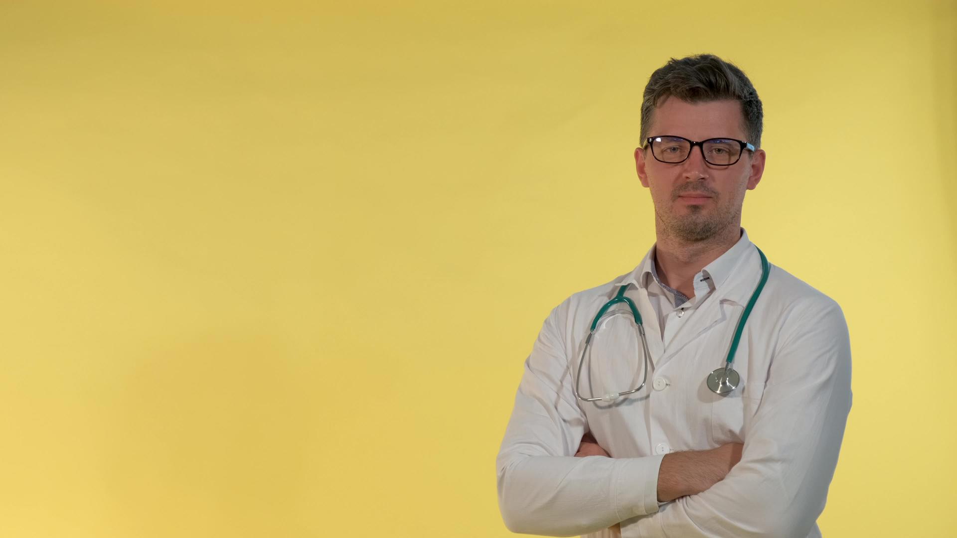 穿着实验室外套的帅哥医生对着黄色背景的相机微笑视频的预览图