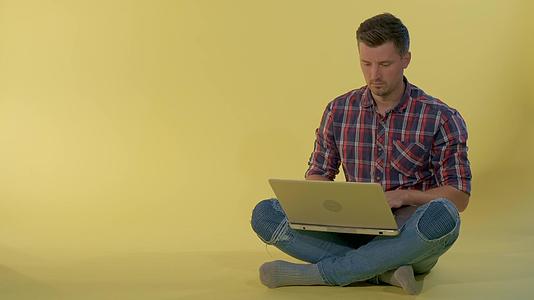 一个迷人的年轻人坐在地板上和电脑上的朋友聊天；视频的预览图