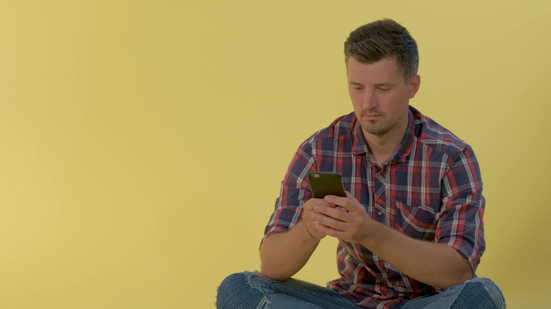 快乐的男人穿着格斗衬衫坐在地板上在智能手机上聊天视频的预览图