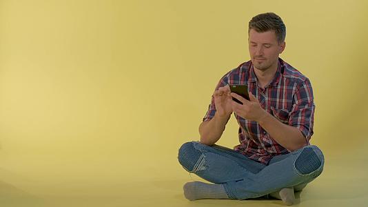 英俊的男孩坐在地板上用智能电话和朋友聊天视频的预览图