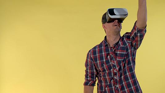 深色头发的男性在黄色背景下站立时使用虚拟现实眼镜视频的预览图