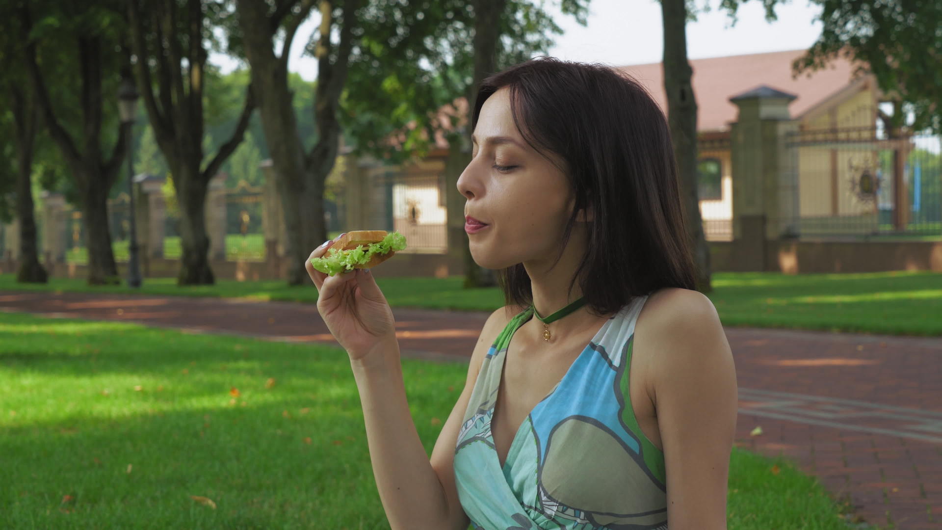 女孩坐在公园的地上吃三明治视频的预览图