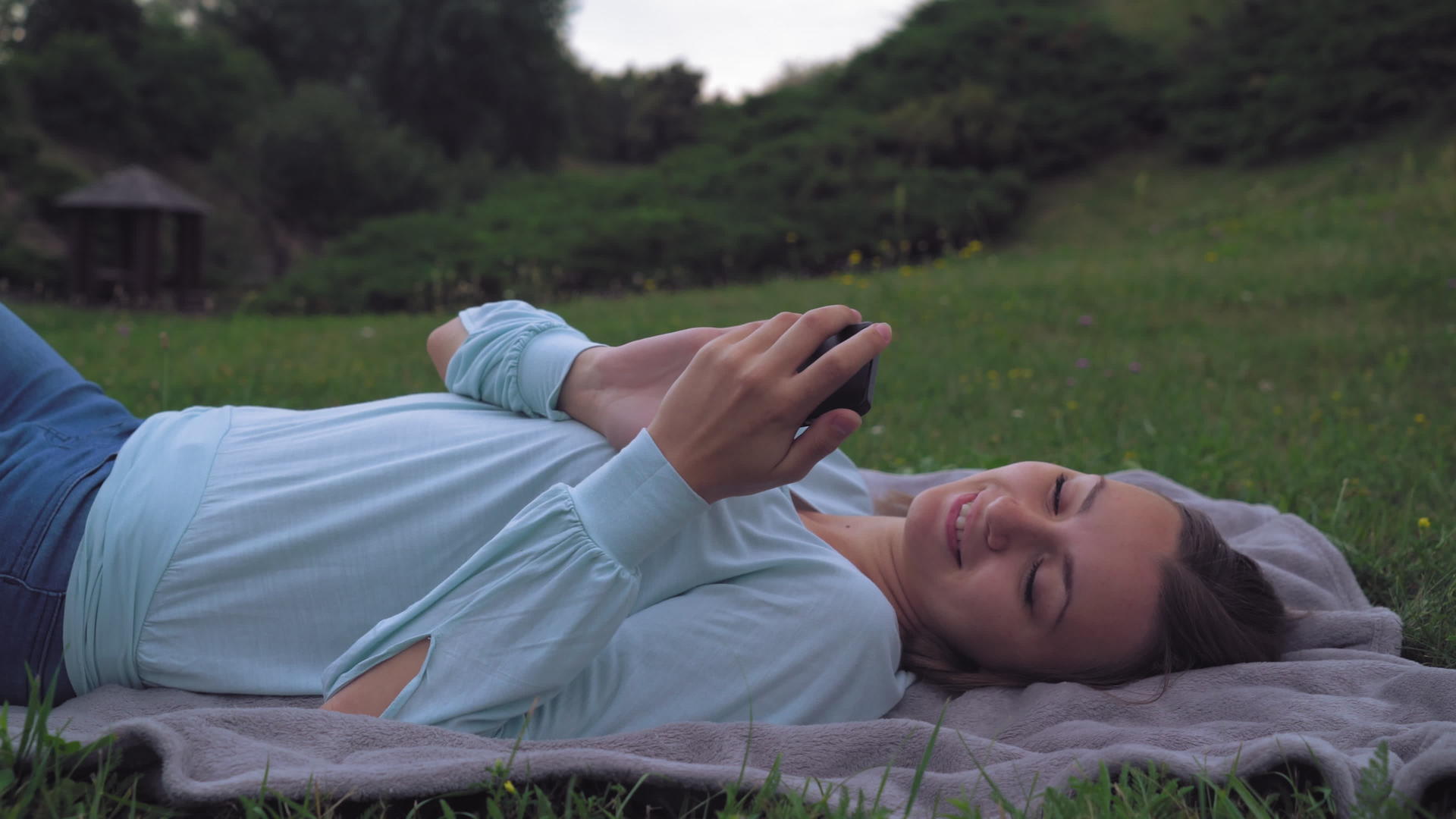 小女孩躺在公园的草坪上在手机上收到一条信息然后闭上眼睛视频的预览图
