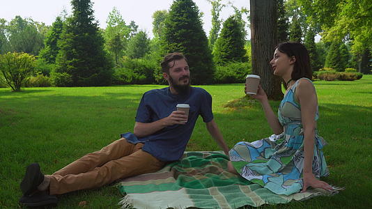男孩和女孩坐在公园里在地上聊天喝咖啡杯视频的预览图