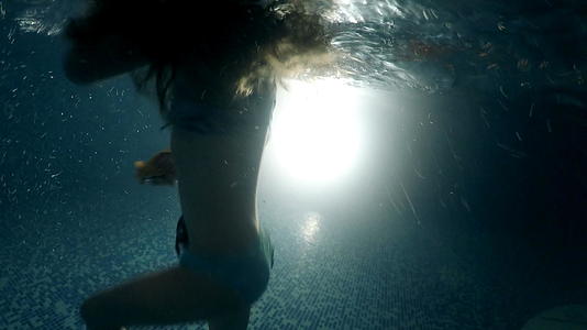 小女孩在黑暗的游泳池下游到明亮的月光下视频的预览图