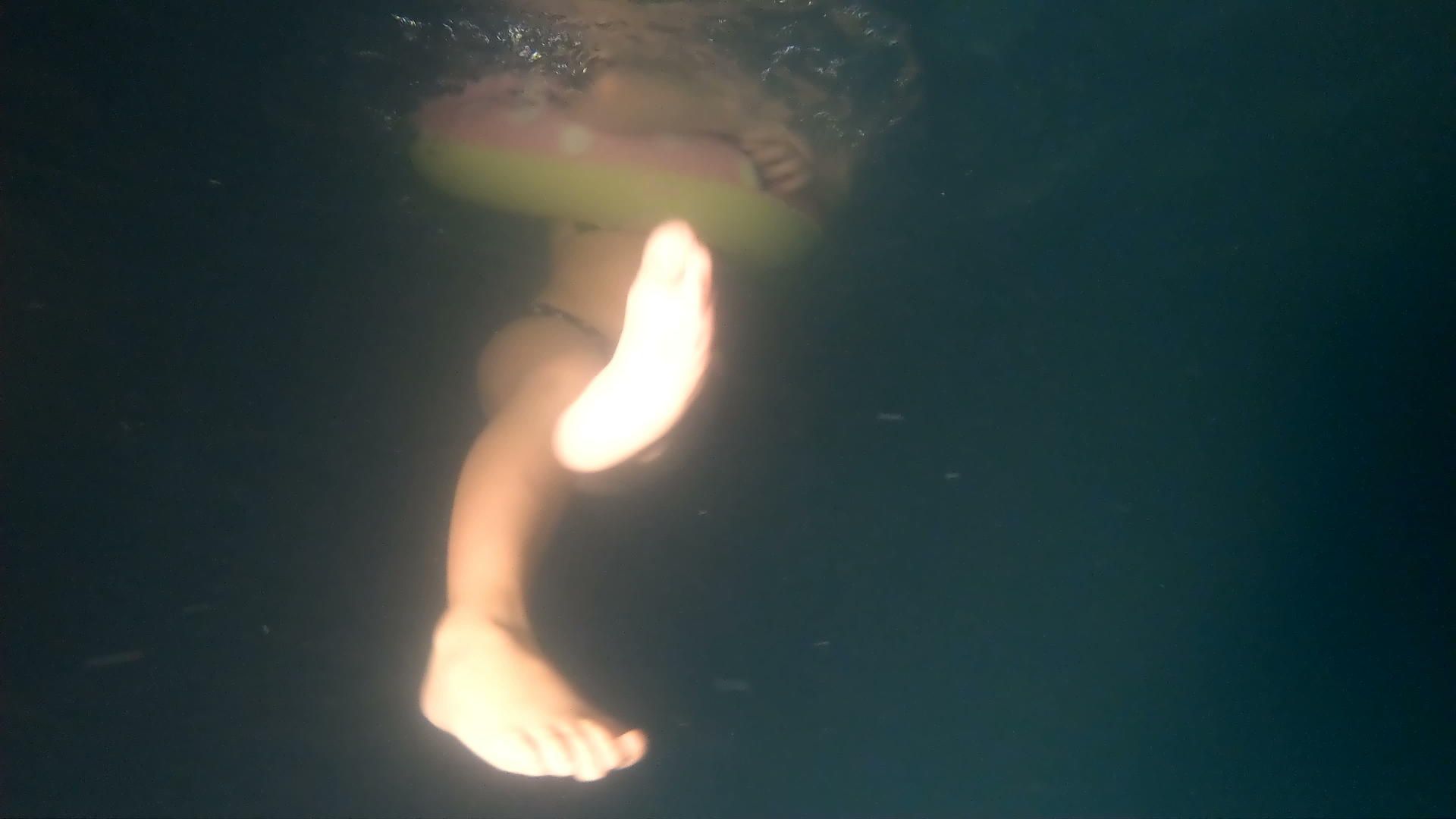 带着充气环的小女孩在暗泳池水下慢动作中旋转视频的预览图