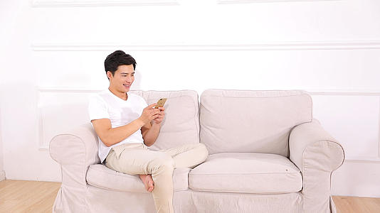 居家男青年在沙发上使用手机视频的预览图