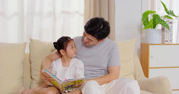 8K爸爸陪女儿坐在沙发上看故事书视频的预览图