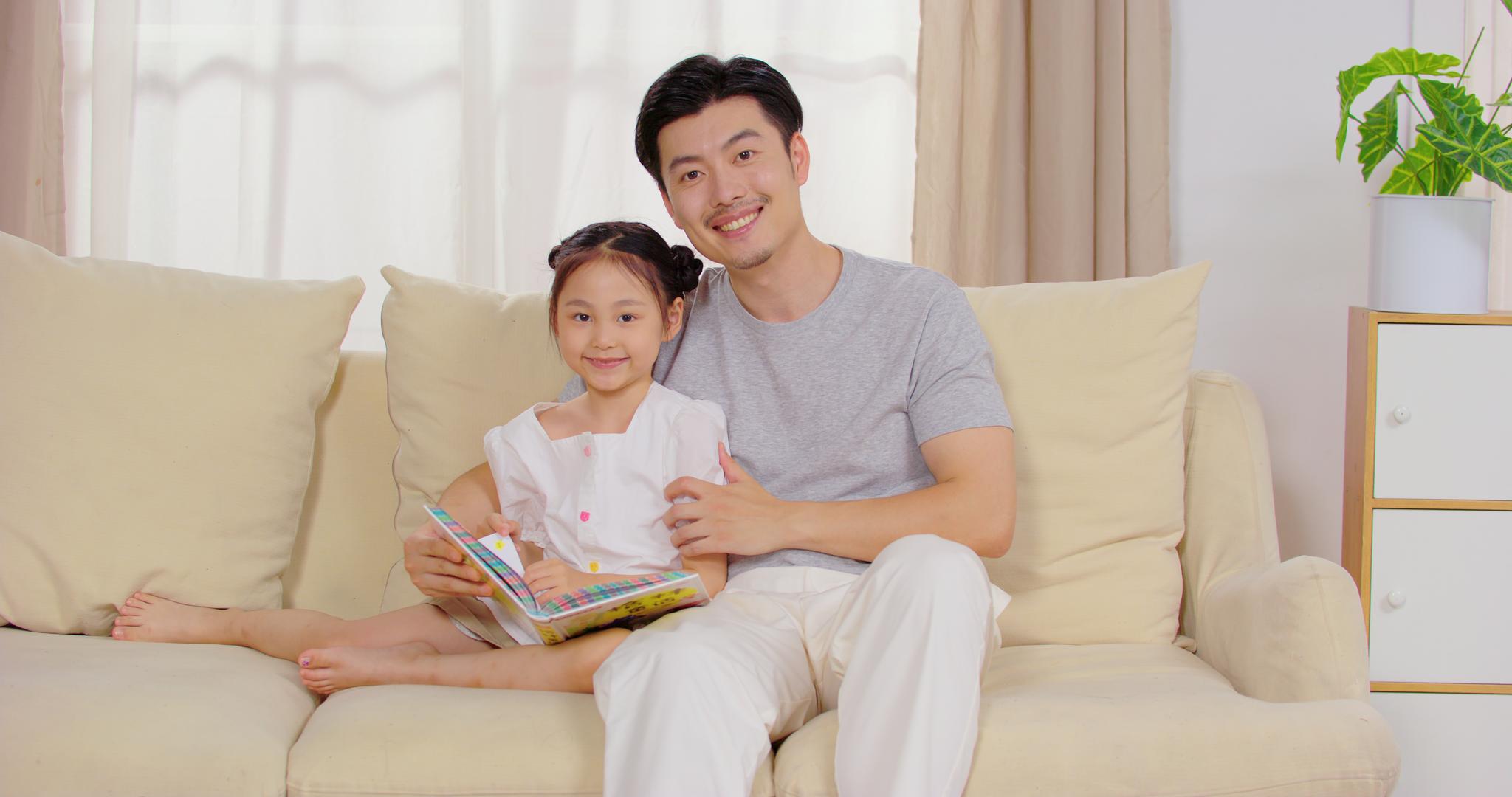 8K爸爸陪女儿坐在沙发上看故事书视频的预览图
