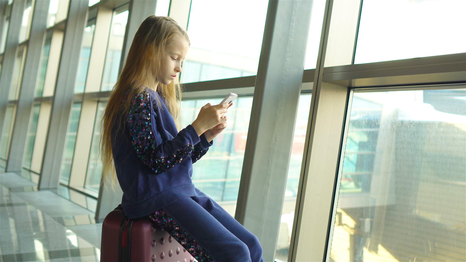 机场里可爱的小女孩在大窗口附近玩手机视频的预览图