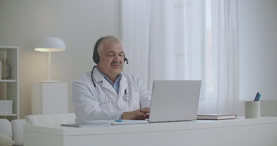 白发医生利用办公室的笔记本电脑通过互联网在网上聊天视频的预览图