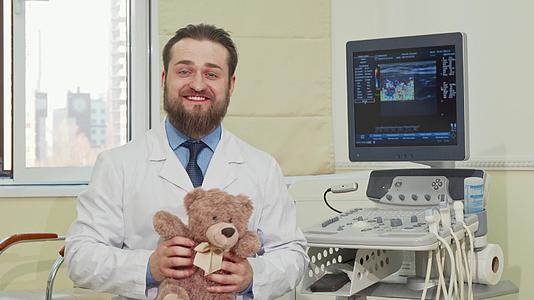 一位友好的男儿科医生拿着泰迪熊玩具向相机挥手视频的预览图