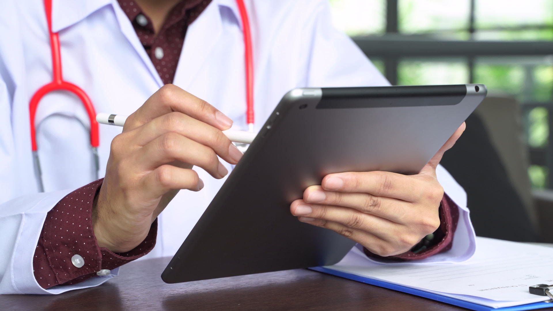 医生正在用平板电脑近距离用听诊器拍摄治疗报告视频的预览图
