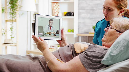 躺在医院床上的老年残疾妇女通过在线视频电话与医生沟通视频的预览图