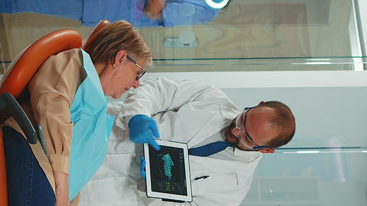 垂直视频医生用平板电脑向患者展示X光牙齿视频的预览图