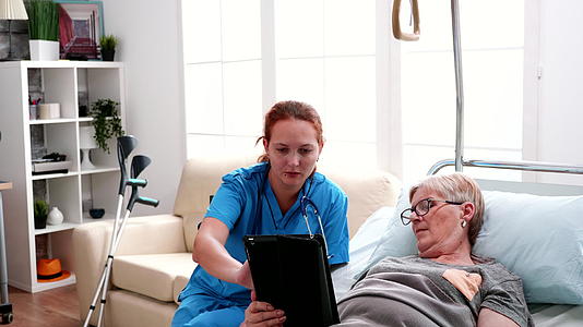 躺在床上的老年妇女向女医生学习如何使用平板电脑视频的预览图