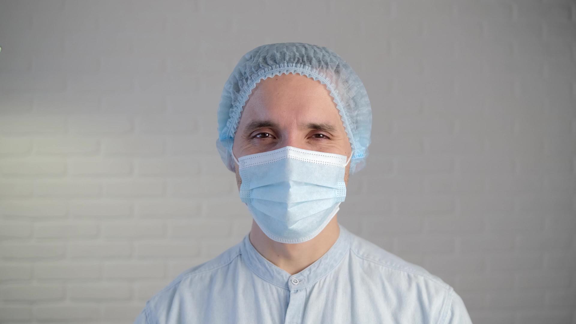 一名疲惫的男性医生在疾病期间戴着保护性口罩医生通过视频的预览图