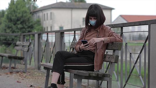 在3号公园戴着医用口罩的年轻女孩看着她的智能手机视频的预览图