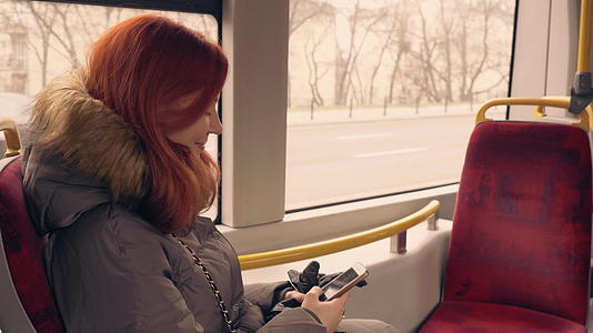 美丽快乐的女孩在公共交通中使用智能手机视频的预览图