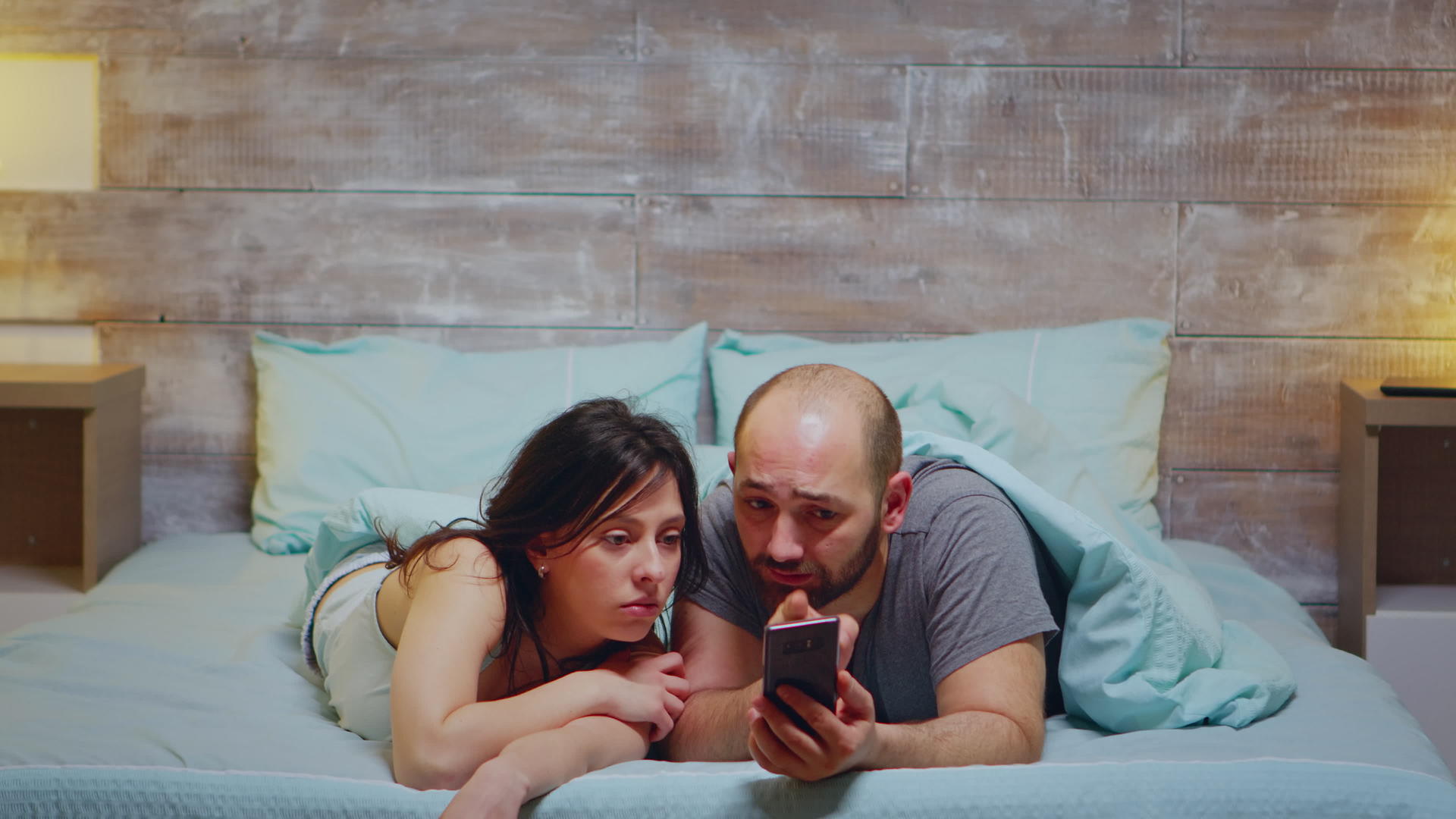 丈夫和妻子穿着睡衣躺在床上时使用电话视频的预览图