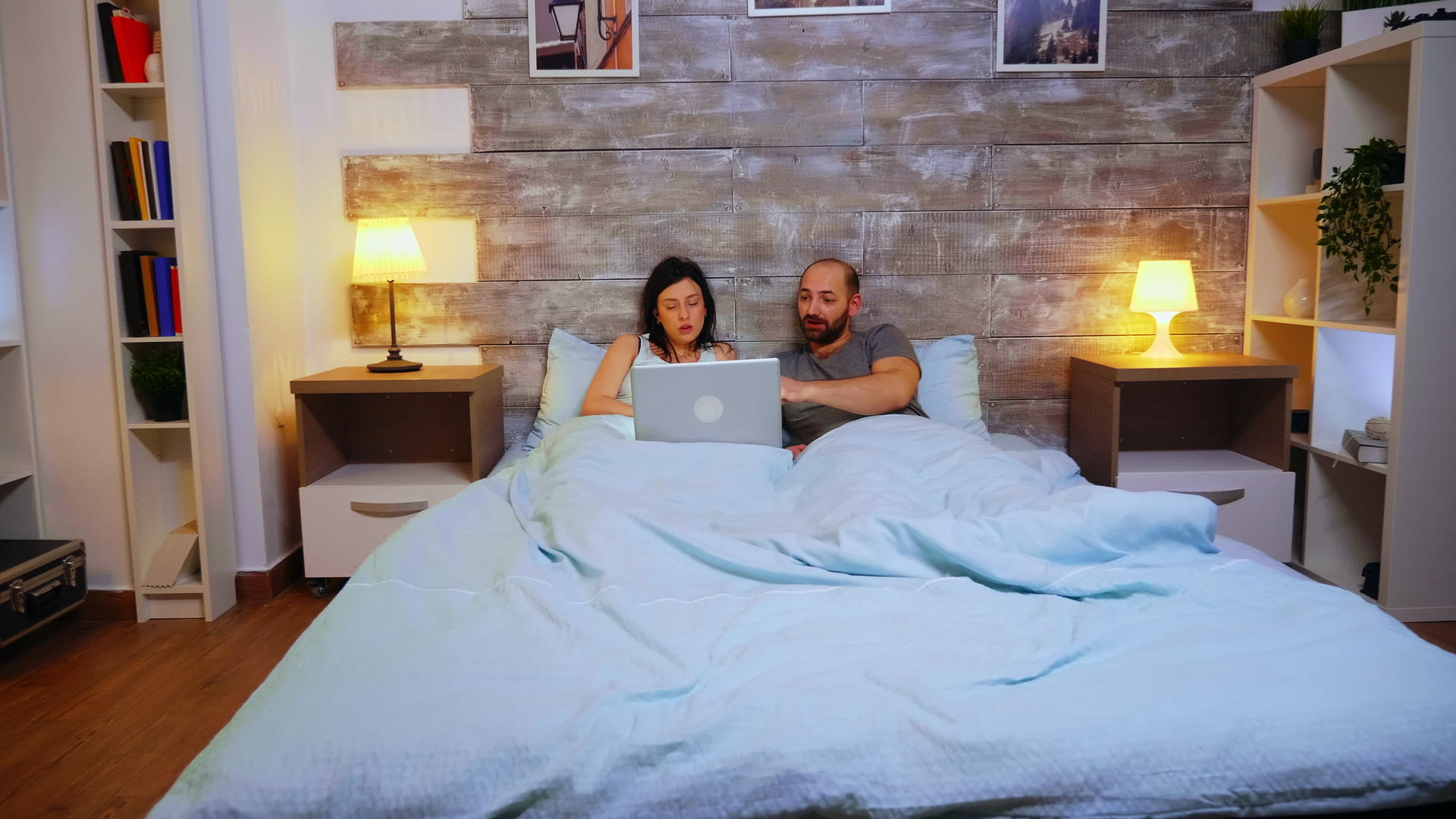 一对夫妇用笔记本电脑躺在毯子下的床上视频的预览图
